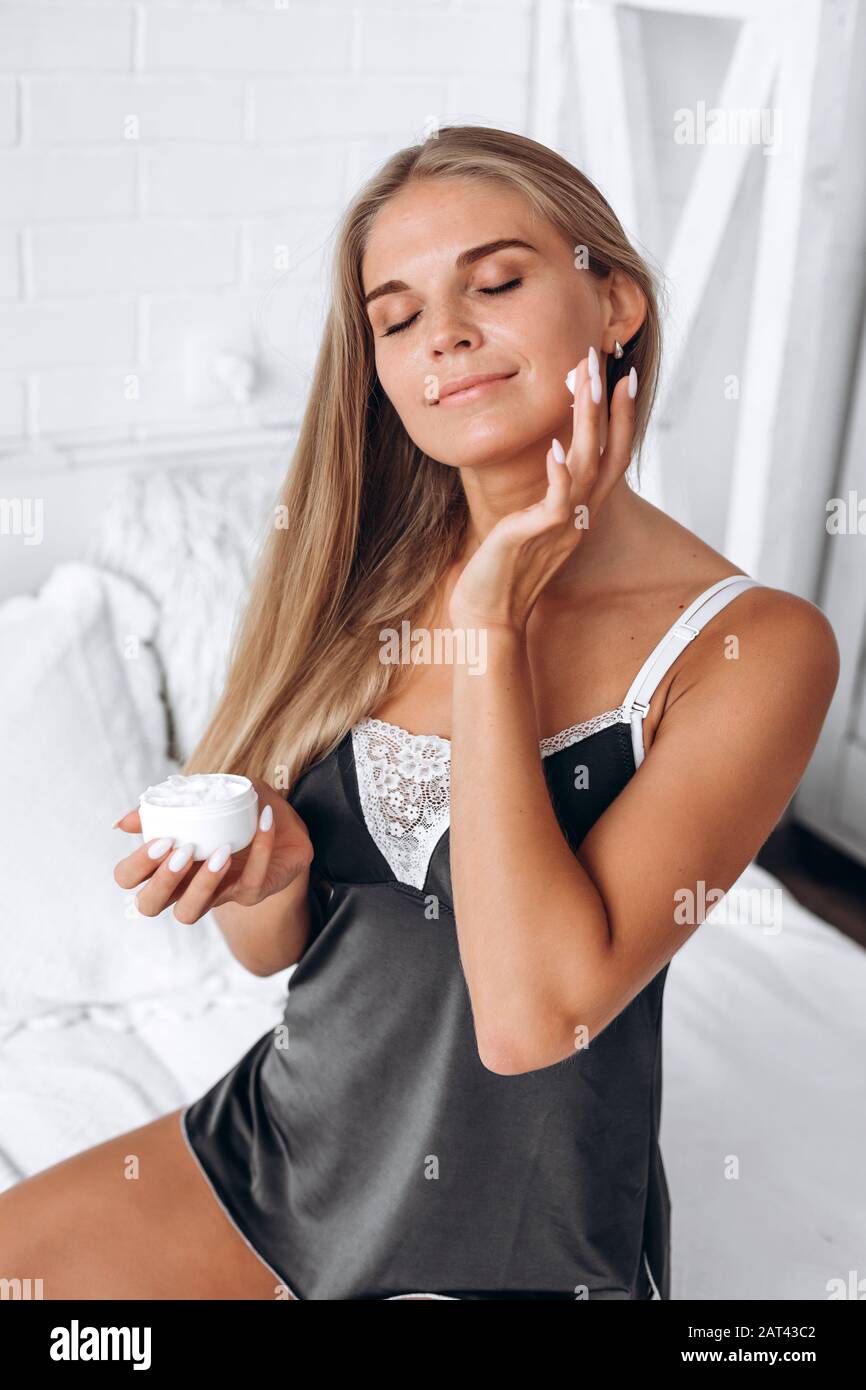 Woman in black pajamas applies cream on face Stock Photo