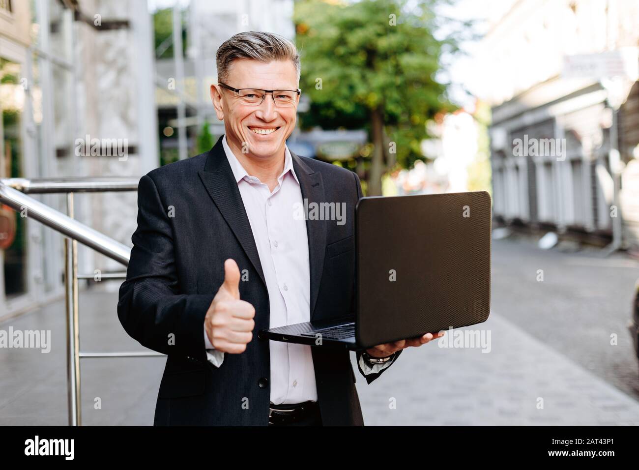 Happy businessman holding open laptop, smiling with thumb up- Image Stock Photo