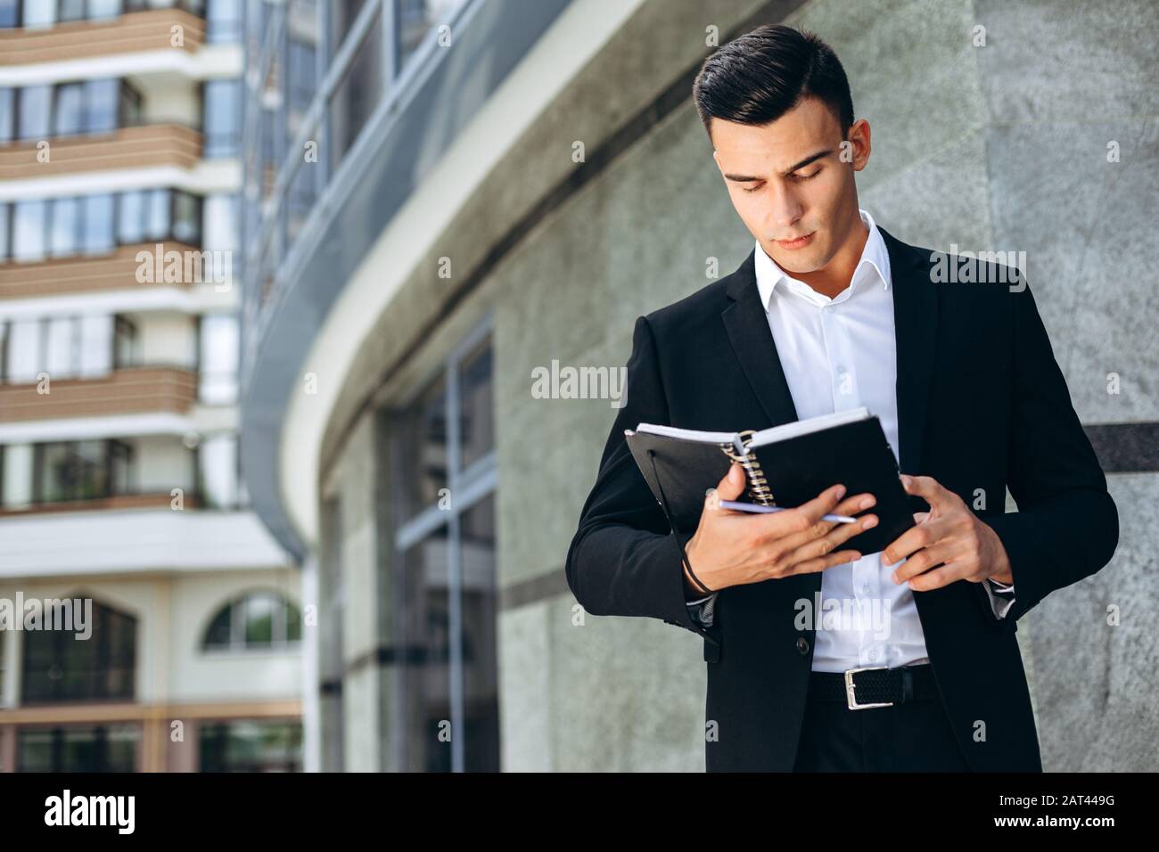 Businessman standing next a business building holding a paper planner and looking in it.- Image Stock Photo