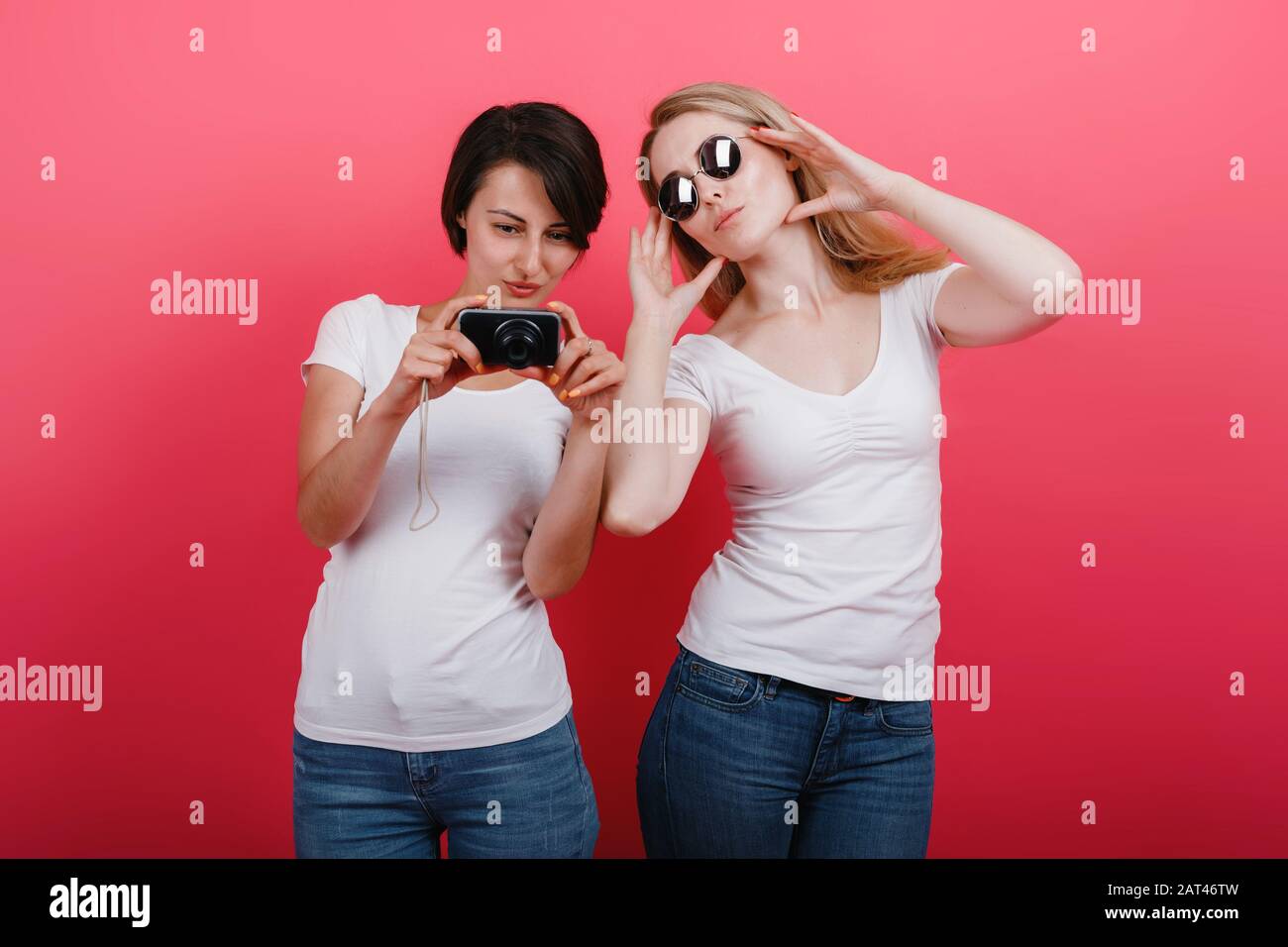 Friendship concept. Woman holding a photocamera and another woman in sunglasses posing in the studio Stock Photo