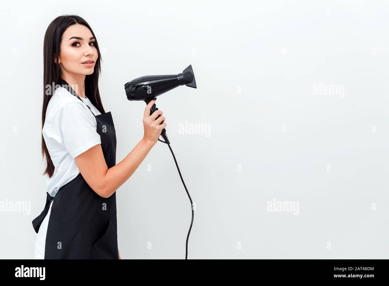 Beautiful girl with long dark hair holds a hairdryer on a white ...