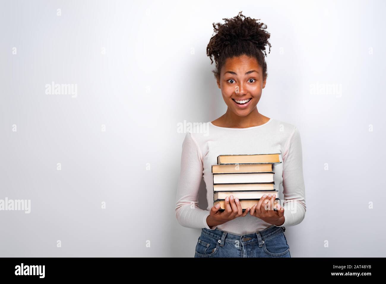 Portrait of an excited young girl holding books over white background ...