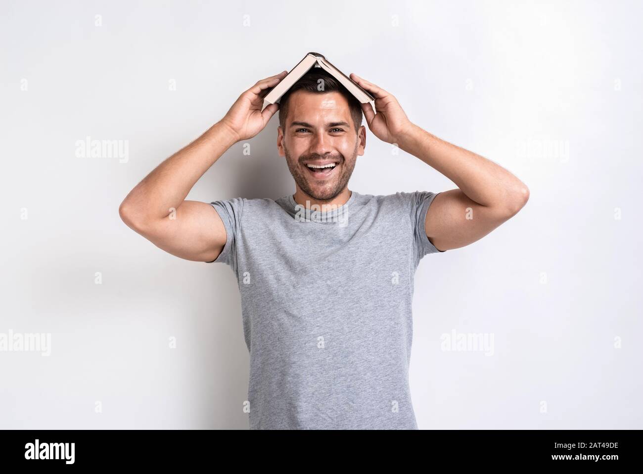 Funny man put the book on his head and happily looking at the camera.- Image Stock Photo