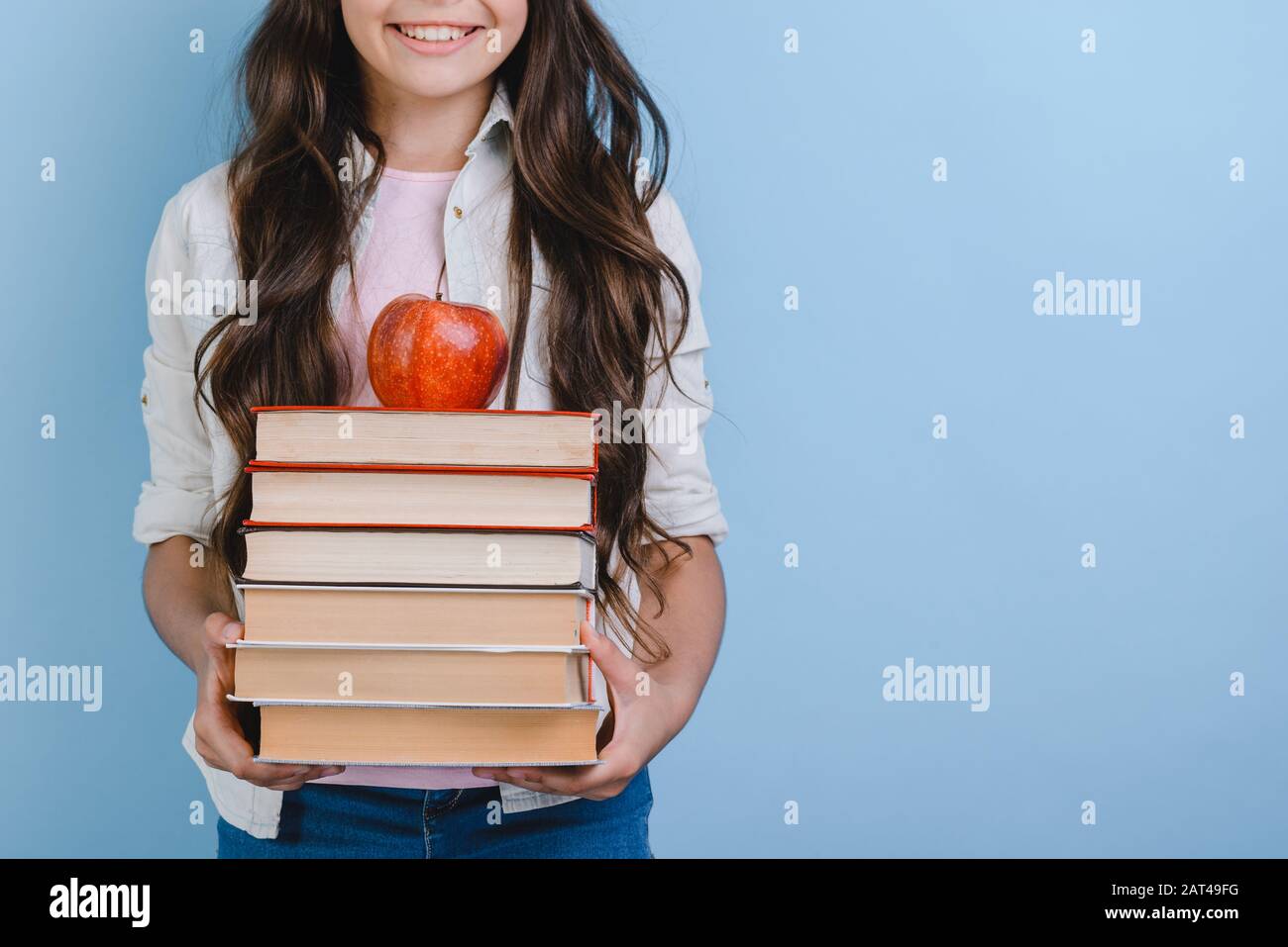 Cropping image of young girl holding stack of books with apple on it ...