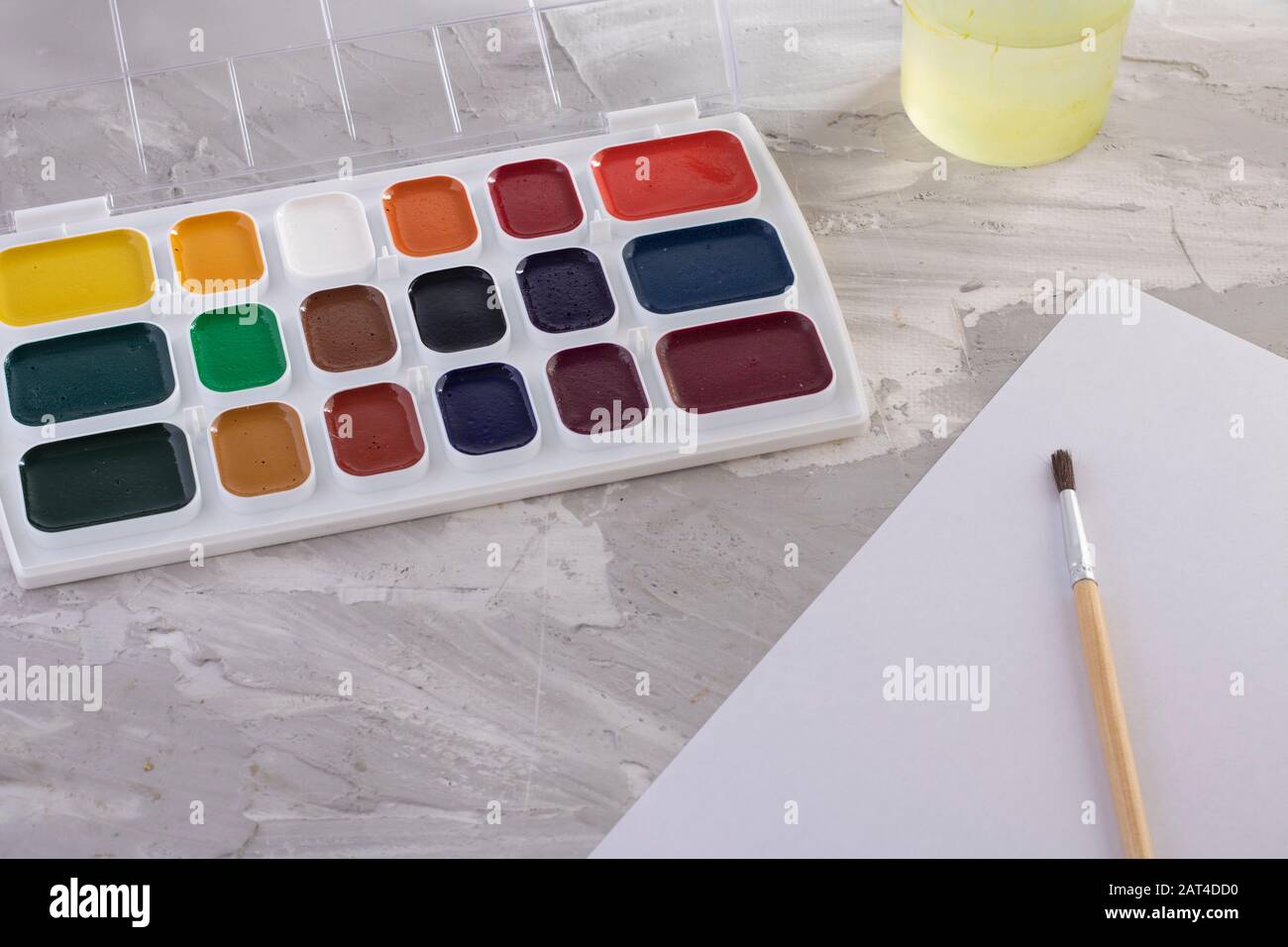 Paints, one brush and water on gray table Stock Photo