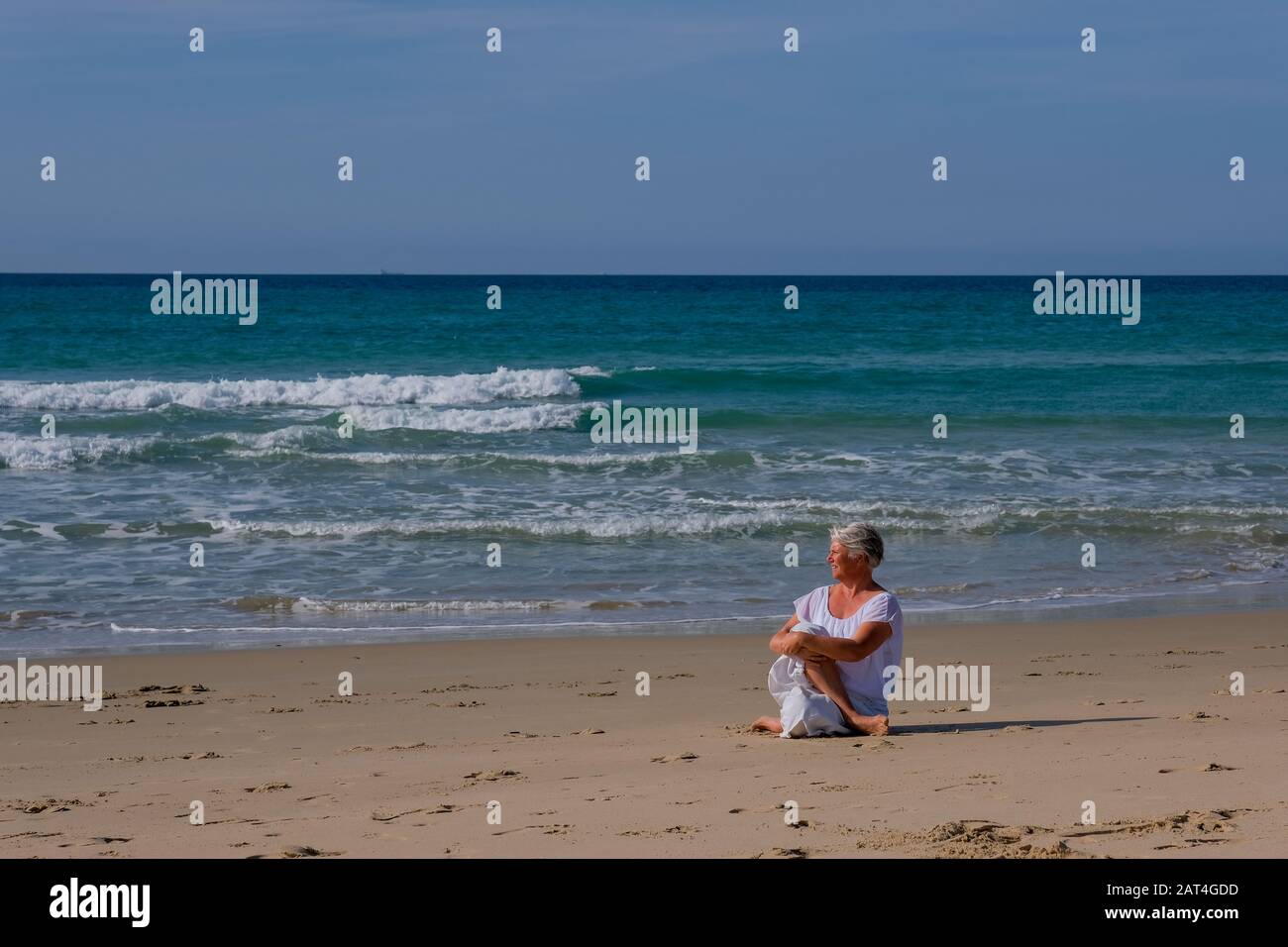 Senior woman with gray hair and a white dress relaxing on the beach Stock Photo
