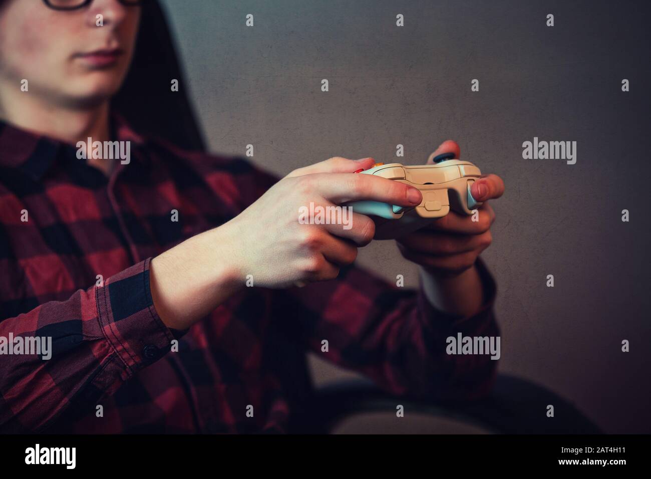 Close up of teenage boy hands playing video games holding a joystick console, seated relaxed in his room. Focused guy having fun in the virtual world. Stock Photo