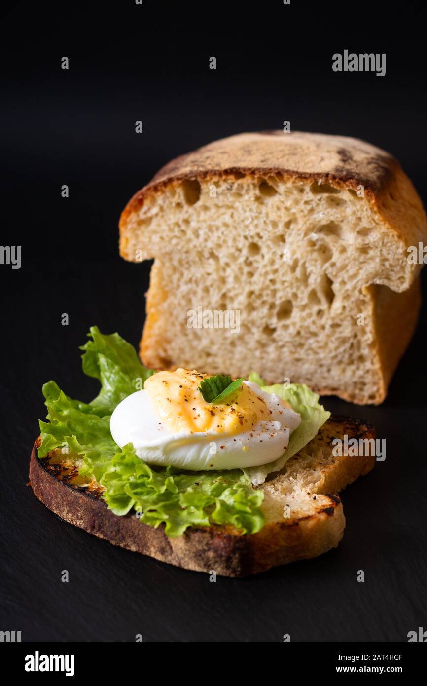 Organic Food breakfast concept homemade Poached egg or eggs benedict on sourdough bread toasted on black slate board Stock Photo