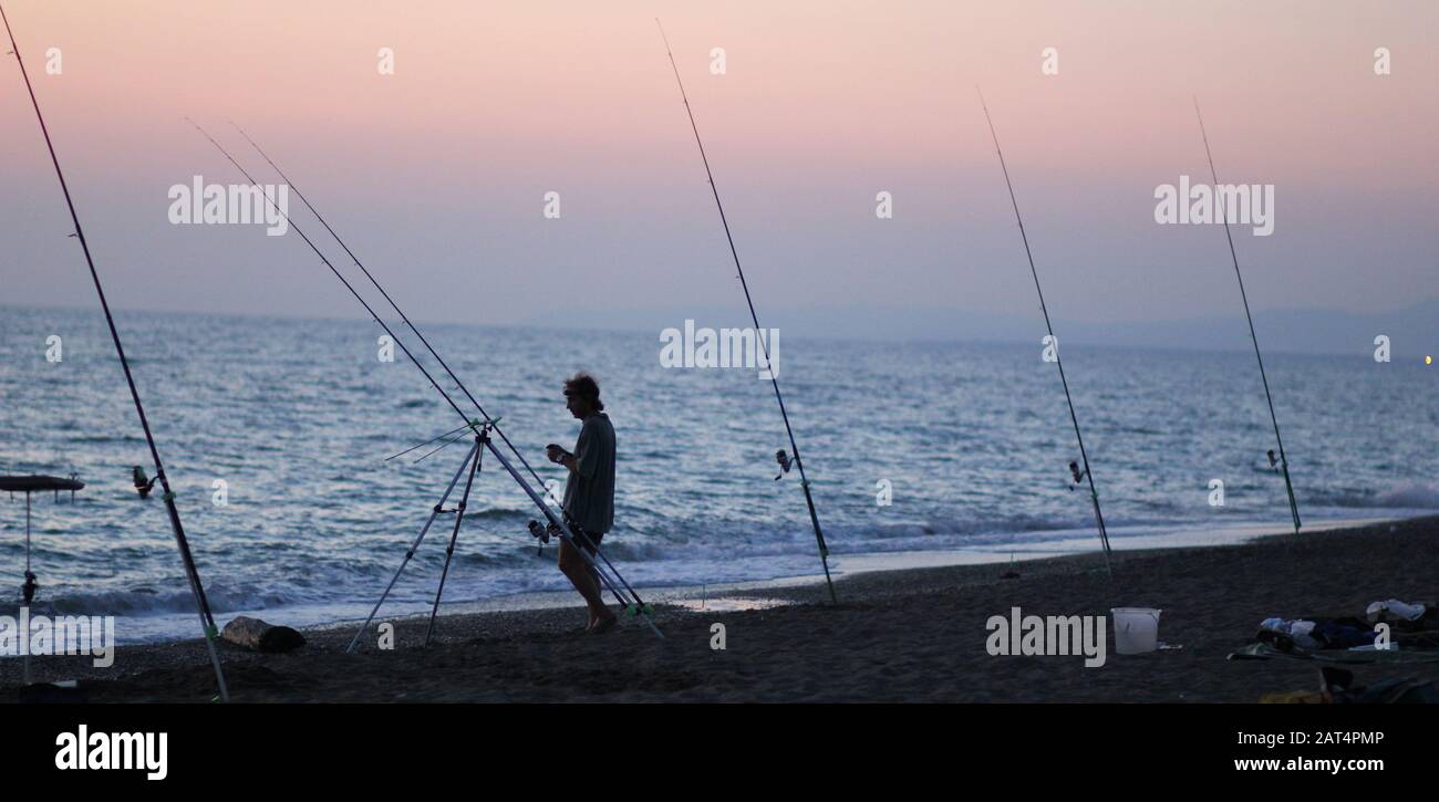 Silhouette of man fishing on the beach at sunset Stock Photo - Alamy