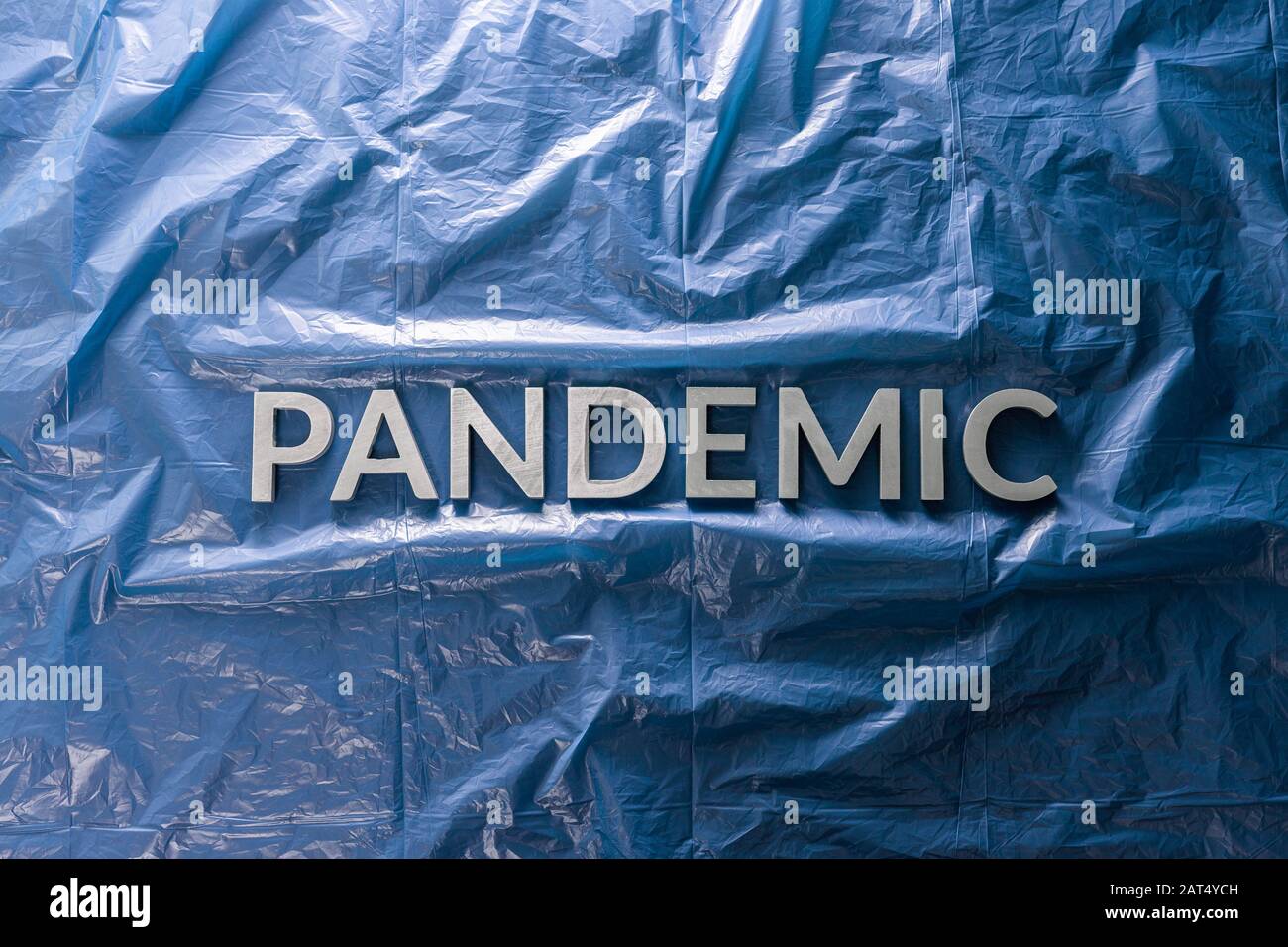 the word pandemic laid with silver letters on crumpled blue plastic film background in flat lay composition at center with dramatic cold light Stock Photo