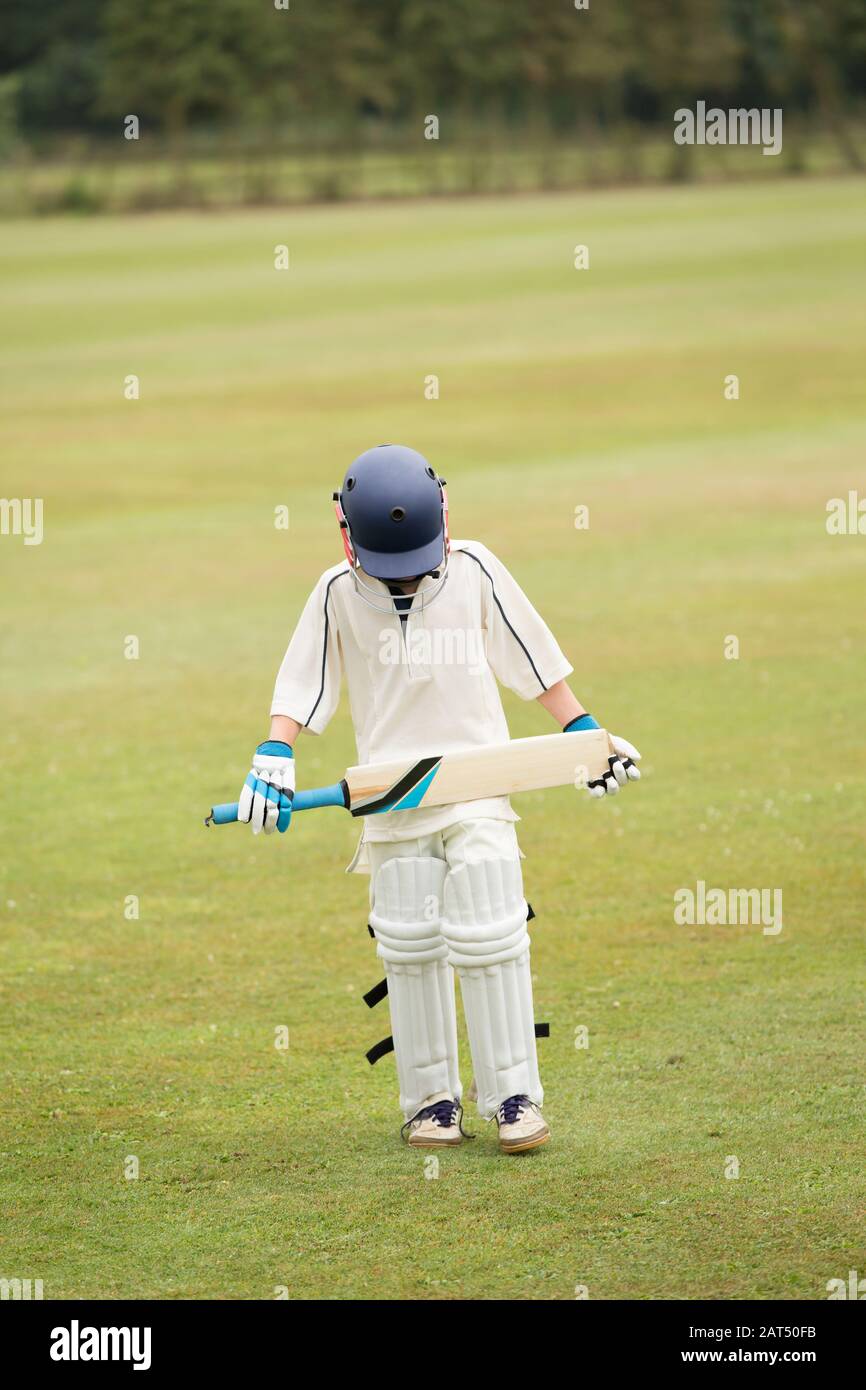 Cricket, a young cricketer with head bowed after defeat, isolated against a green grass background. Stock Photo