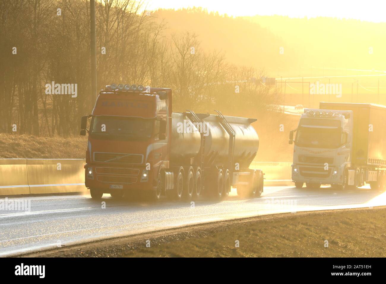 Two Volvo FH trucks, red tanker and white semi pulling freight trailer on wet road in natural, in-camera golden light. Salo, Finland. January 24, 2020 Stock Photo