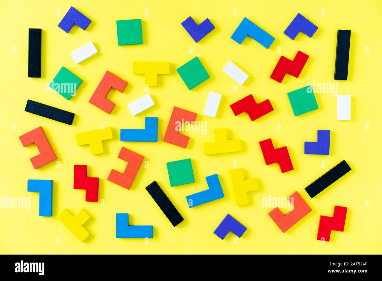 Colorful wooden blocks of different shapes puzzles on yellow background. Natural, eco-friendly toys. Creative, logical thinking concept. Background with geometric shapes wooden blocks. Stock Photo