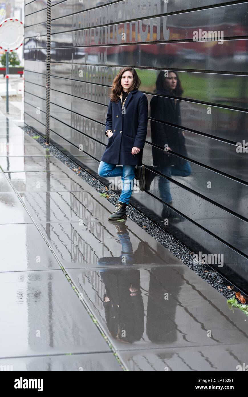 Woman reflecting four times in a contemporary black metal building and in the rain Stock Photo