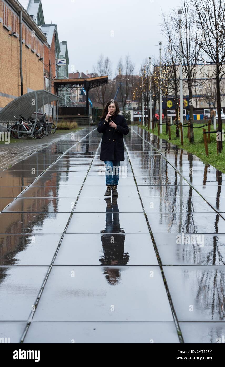 Attractive young white smoking woman walking over a rainy wet pedestrian surface Stock Photo