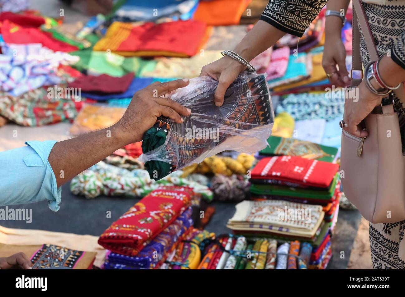 Seller hand in close up view handing over sold dress material to female buyer at a handicraft fair at Bolpur, West Bengal, India Stock Photo