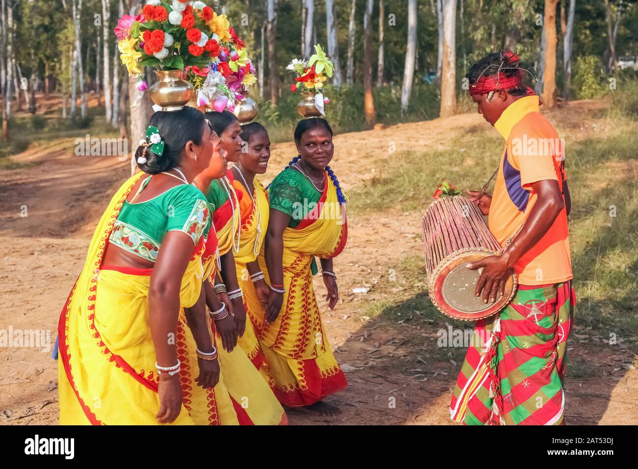 Tribal man plays a musical instrument while women perform folk dance in a forested area at Bolpur Shantiniketan, West Bengal Stock Photo