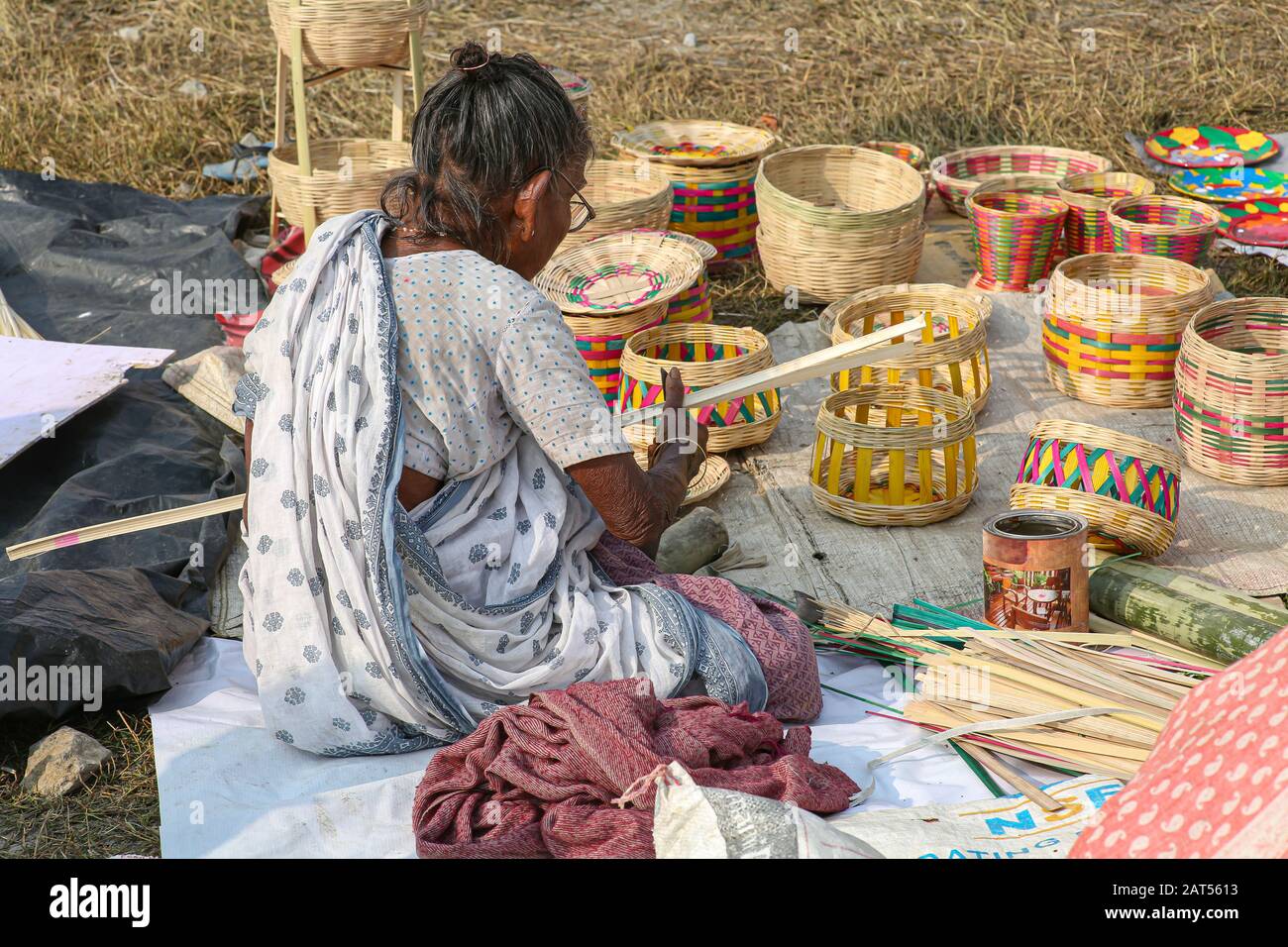 Old woman slicing bamboo cane strands for making baskets to sell for a living at a village in Bolpur, West Bengal, India Stock Photo