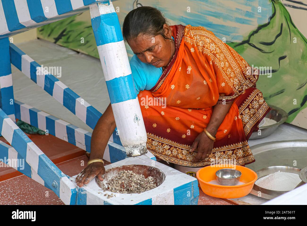 Rural Indian woman grinding rice with a manual operated machine at a village in Bolpur West Bengal, India Stock Photo