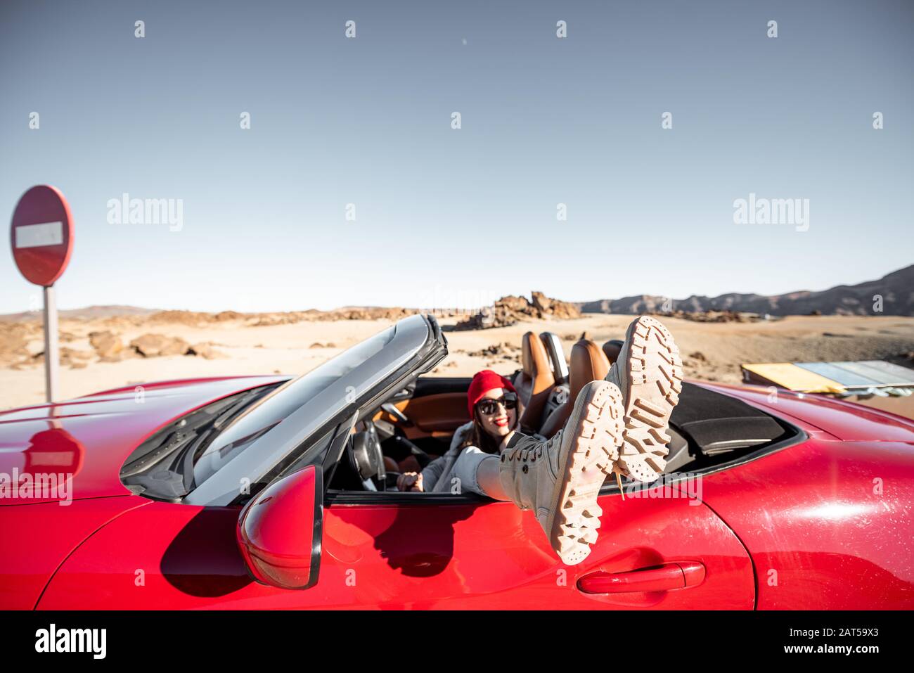 Woman traveling on converrtible sports car, pulling legs out the window