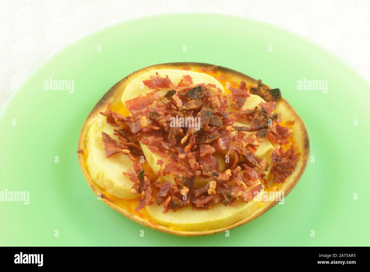 https://c8.alamy.com/comp/2AT5AR5/healthy-snack-of-melted-cheese-apple-slices-and-turkey-bacon-bits-on-tortilla-on-green-plate-with-white-tablecloth-background-2AT5AR5.jpg