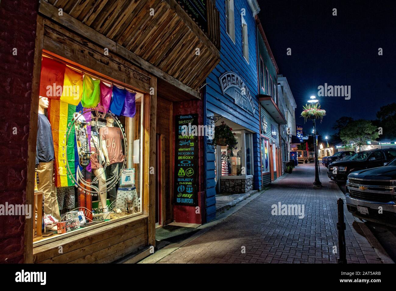 Downtown Little Current at night, with the lighted storefront windows casting a glow onto the cobblestone sidewalk Stock Photo