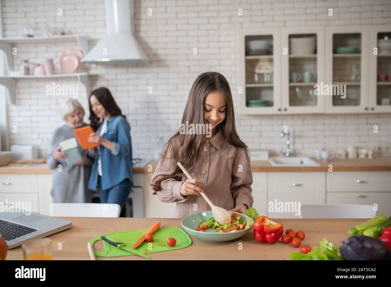 Little girl stirring vegetable salad a big spoon. Stock Photo