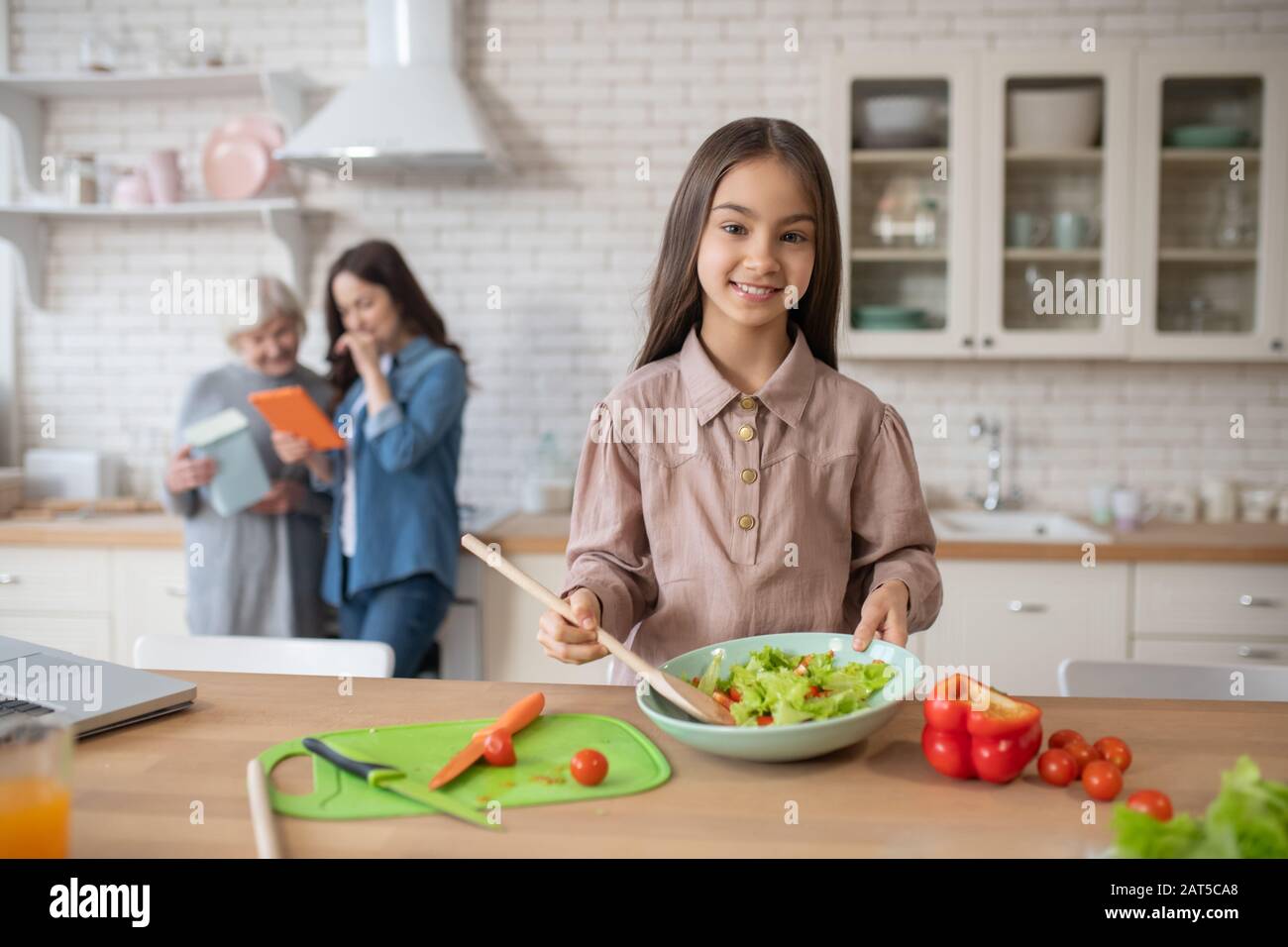 Little girl in the kitchen showing cooked salad. Stock Photo