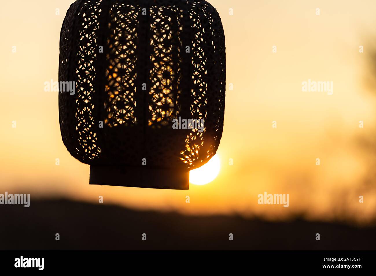 hand holding oriental lantern with candle while sunset. Sun is shining through the lamp. Stock Photo