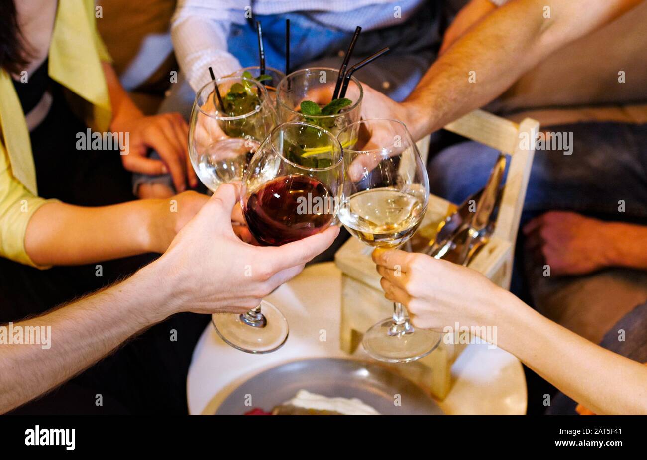 Group of friends are clink glasses with drinks at cafe. They are chatting and having fun Stock Photo