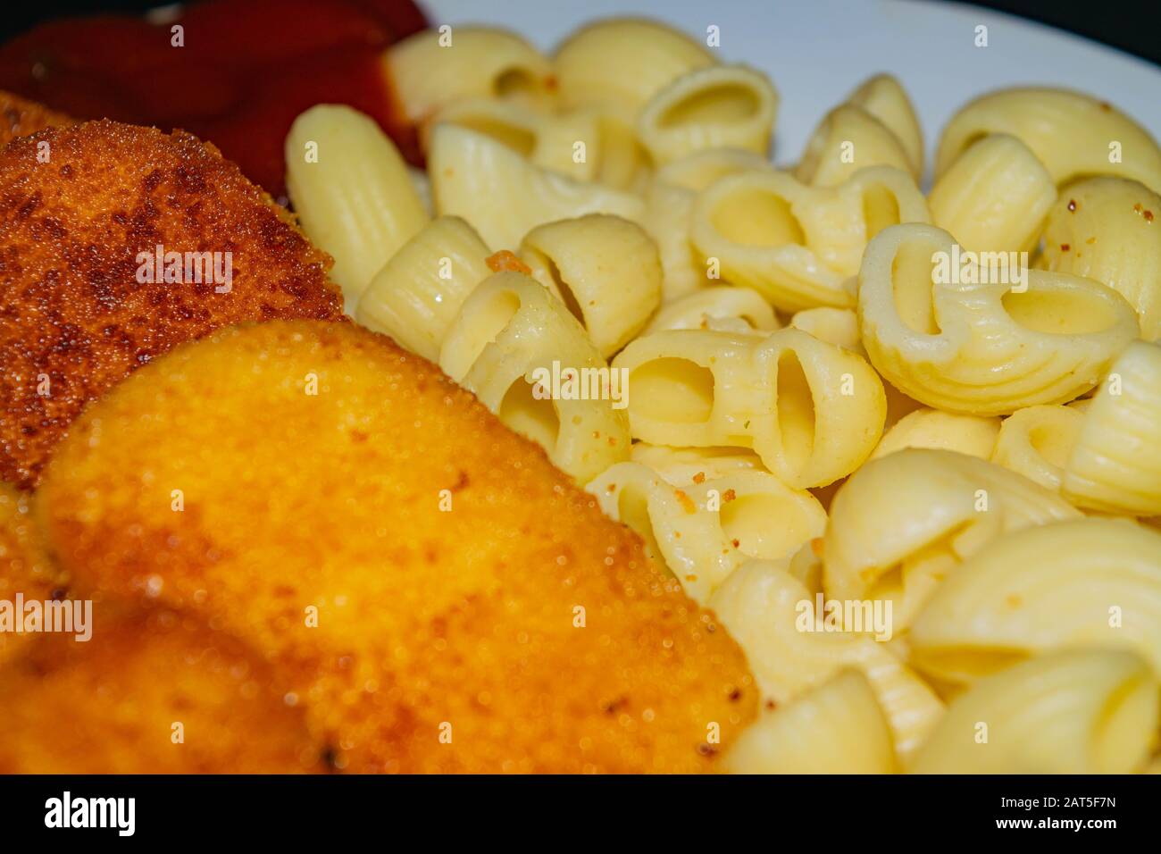 Fried chicken nuggets and cooked pasta on a plate. Close up Stock Photo