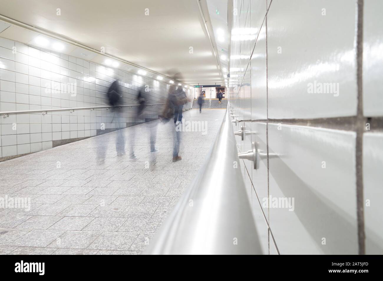people in motion blur walking down bright white tiled tunnel walkway to subways transit Stock Photo