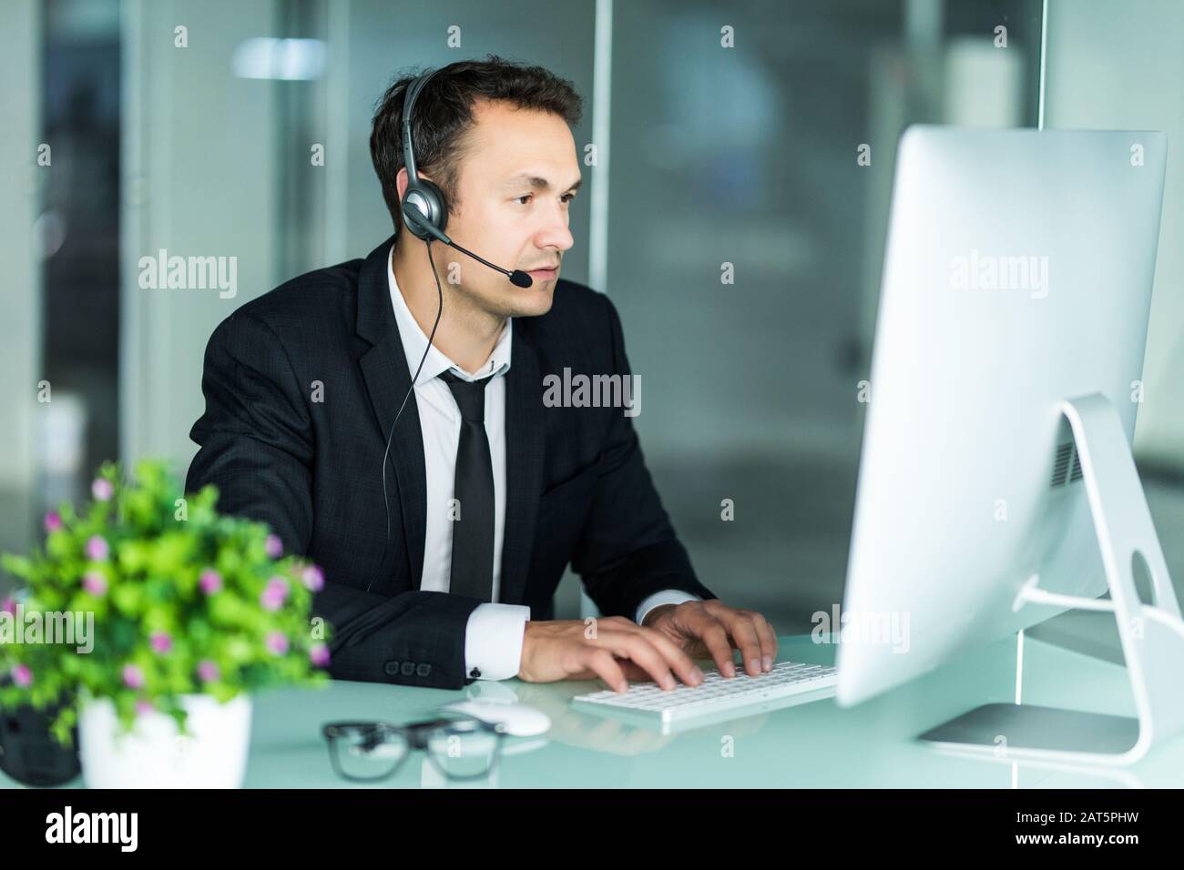 Agent smiling while working on his computer with colleagues next to him Stock Photo