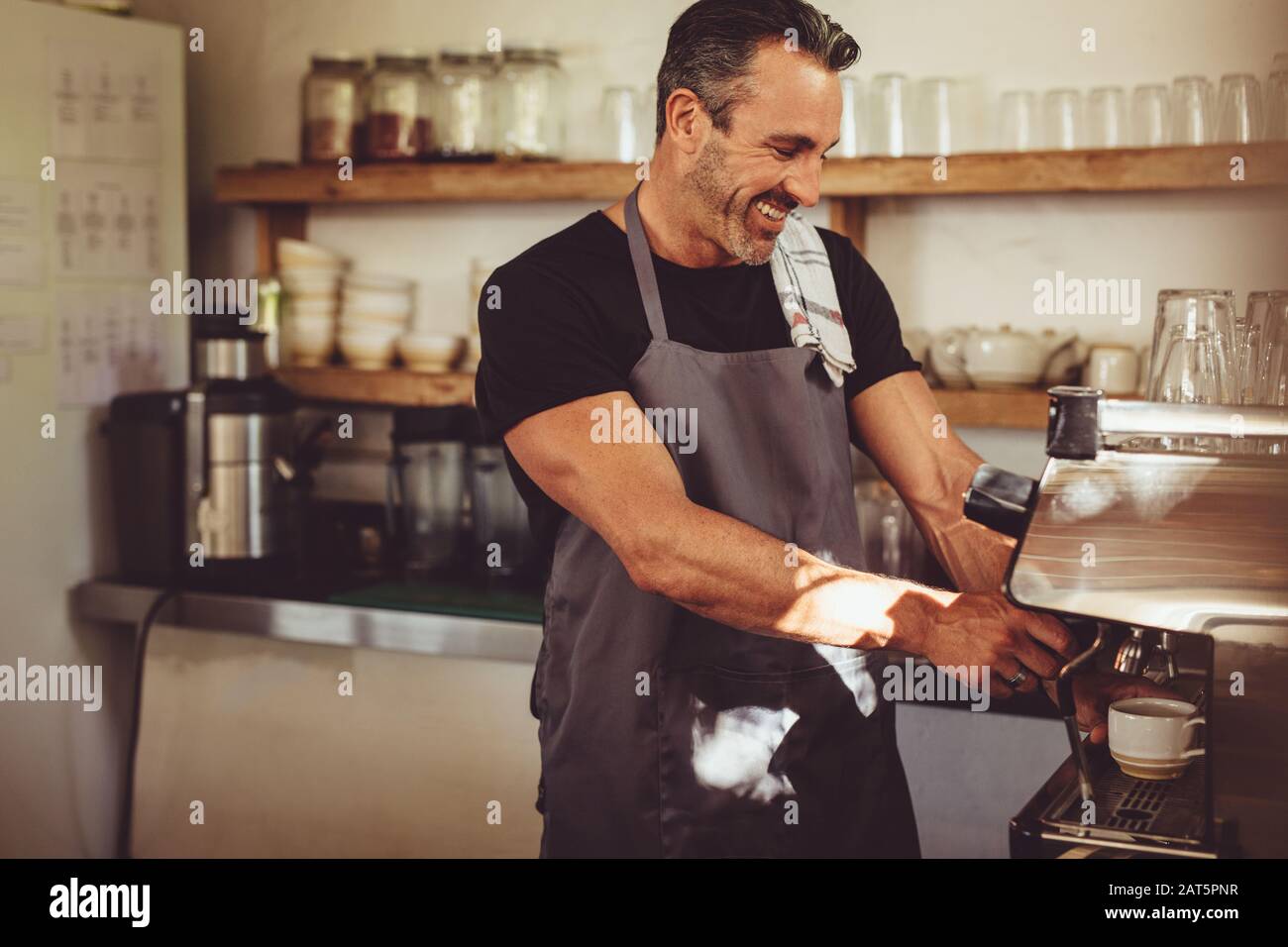 Smiling cafe worker making a cup of coffee with a coffee maker. Male barista working in coffee shop. Stock Photo