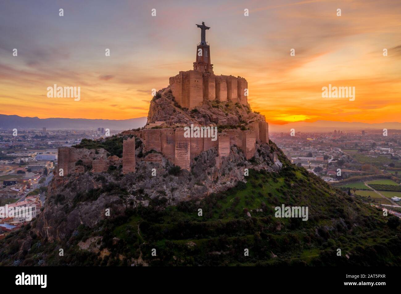 Monteagudo medieval castle ruin twelve rectangular towers circling the hilltop and the sacred heart of Jesus Christ statue on top near Murcia Spain Stock Photo