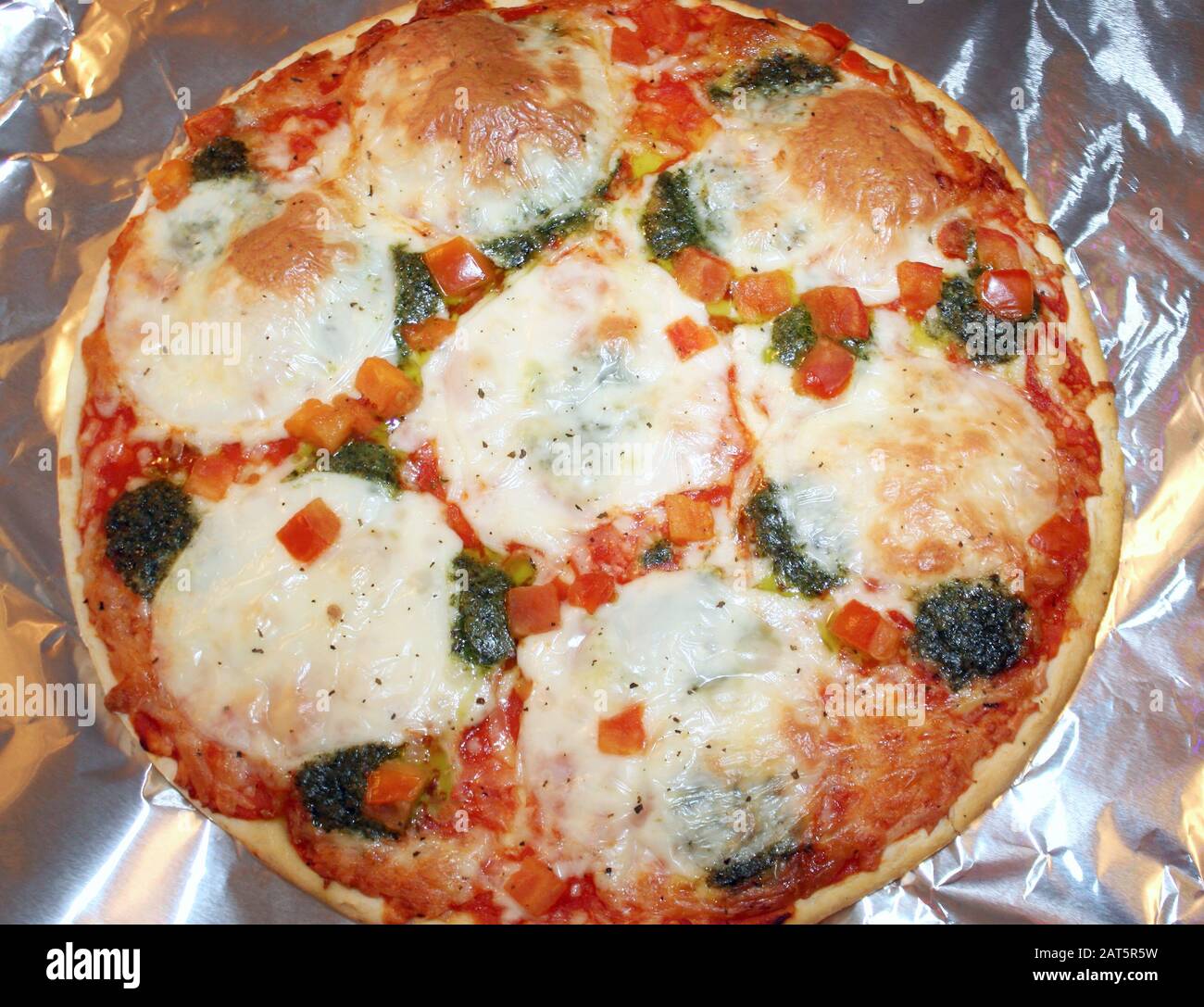 Delicious vegetarian pizza with melted mozzarella cheese cooking on aluminum foil Stock Photo
