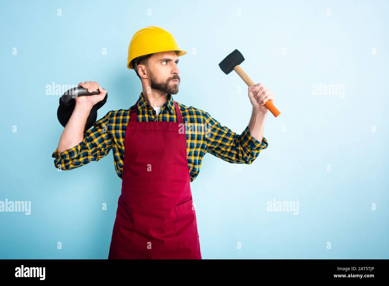 angry bearded workman in safety helmet holding hammer and dumbbell on ...
