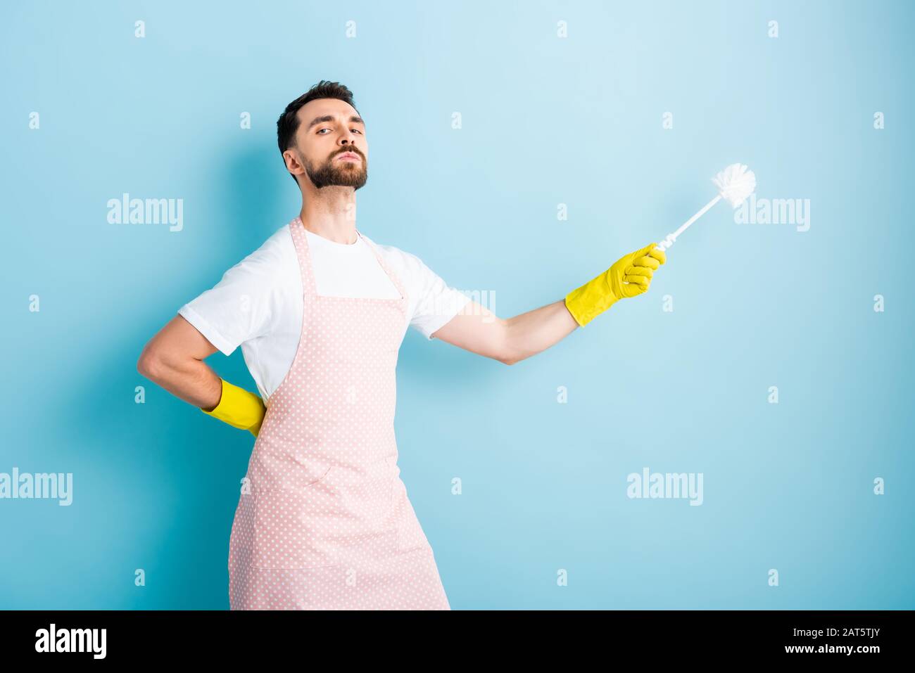 proud man in apron holding toilet brush on blue Stock Photo