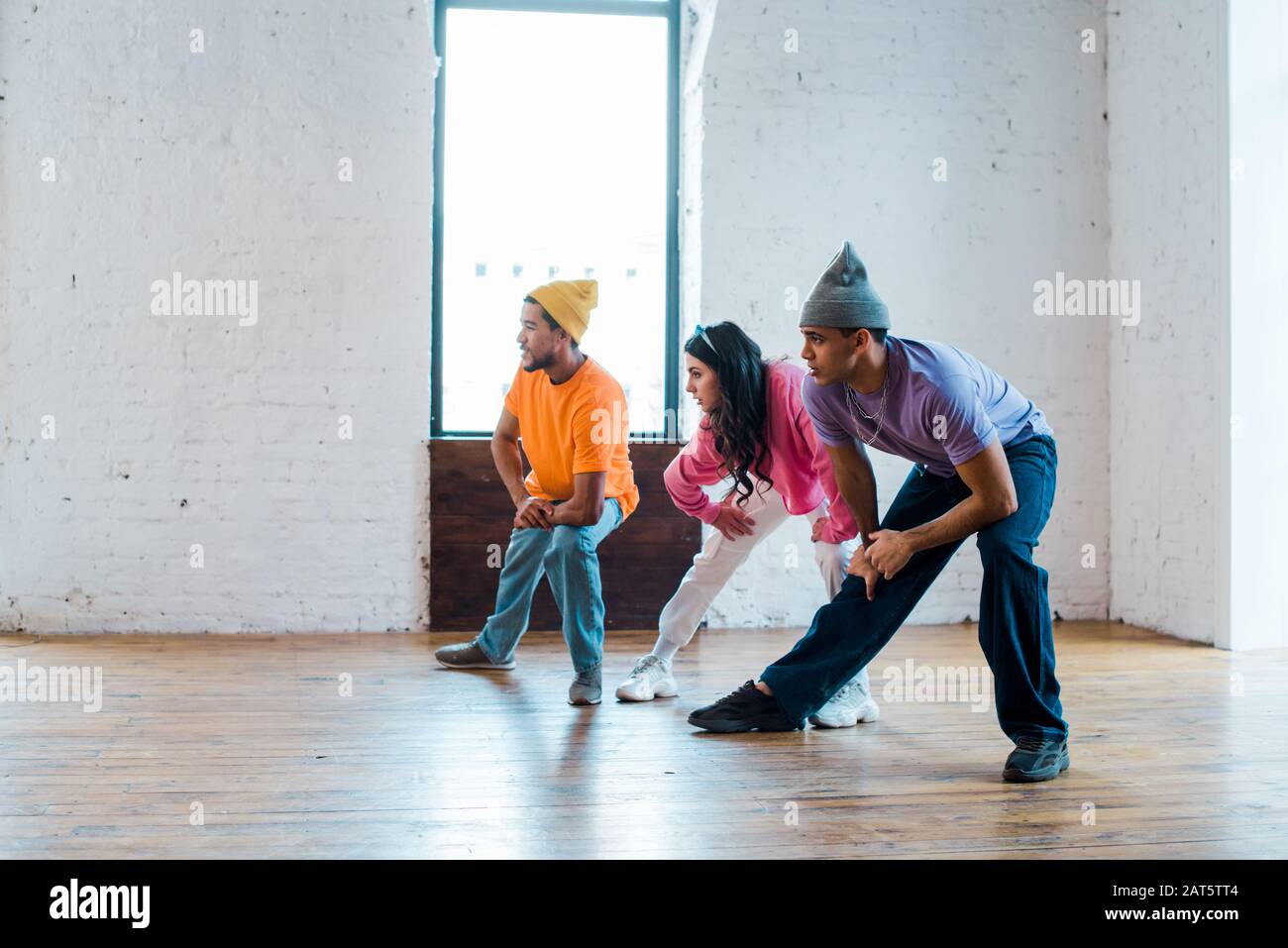 young woman and stylish multicultural men stretching in dance studio ...