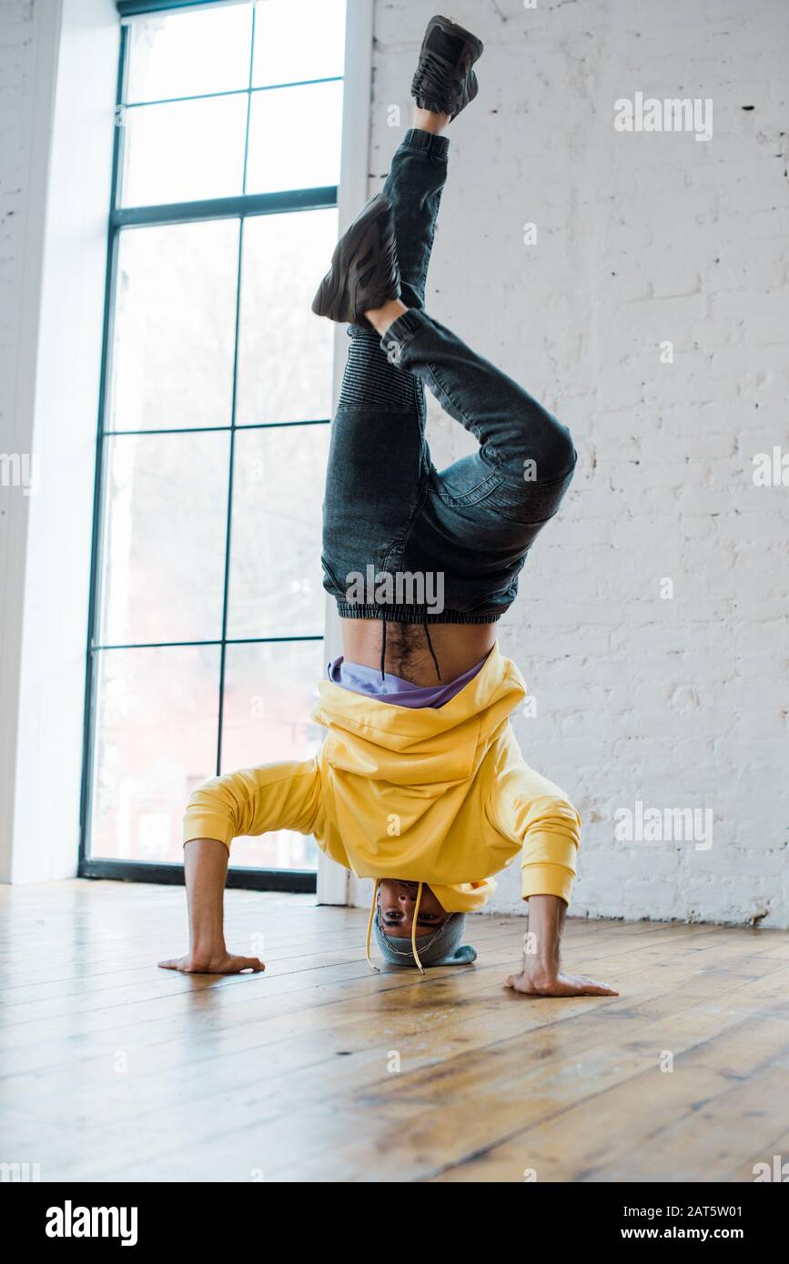 stylish man in hat doing handstand while breakdancing in dance studio Stock Photo