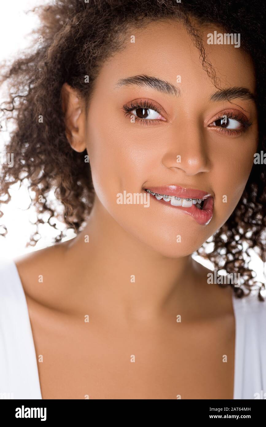 happy african american girl with dental braces biting lip, isolated on white Stock Photo