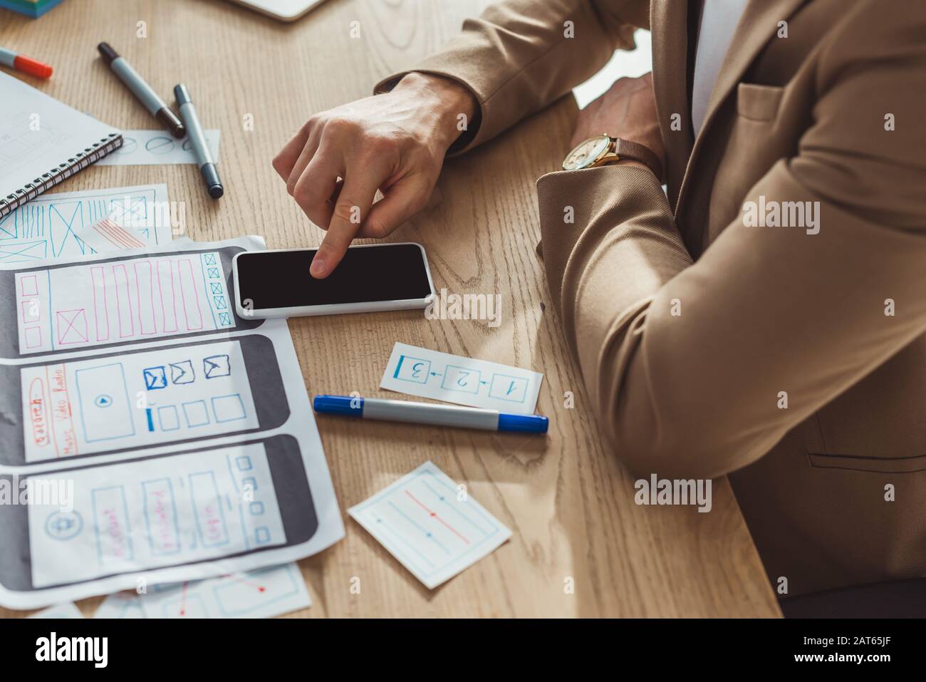 Cropped view of designer using smartphone while developing user experience design at table Stock Photo