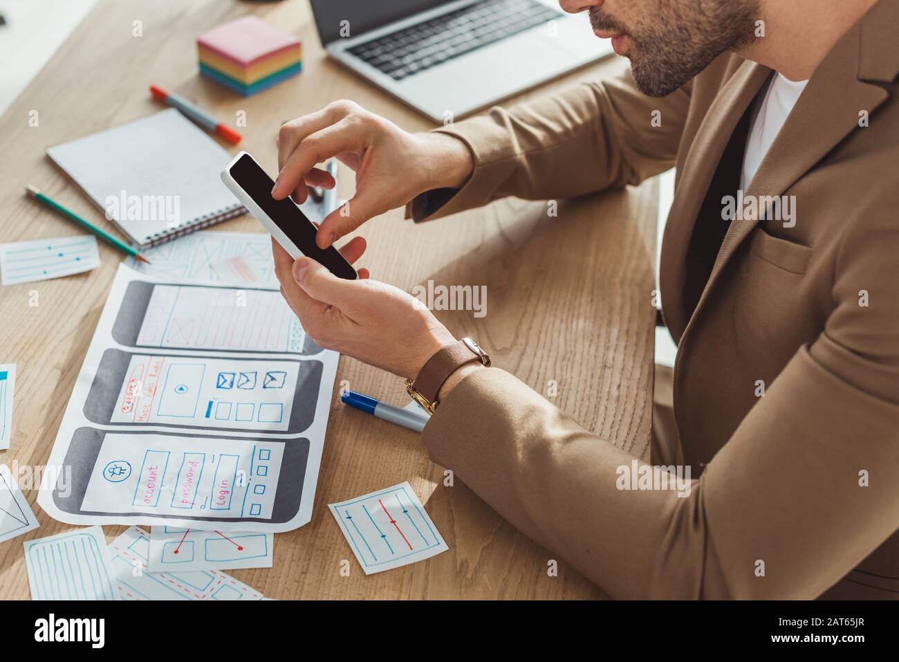 Cropped view of designer using smartphone with mobile web prototype on table Stock Photo