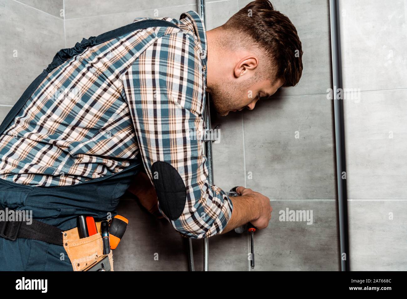 serious installer in overalls standing in bathroom near pipe Stock