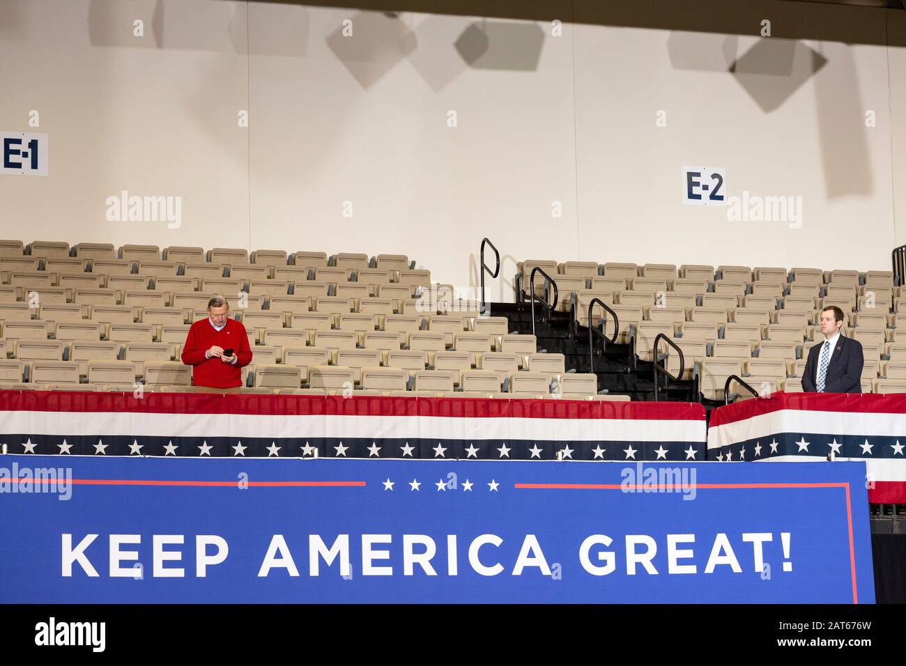 Man in empty seating area with cell phone being monitored by official security as crowd enters to be seated at the 'Keep America Great' rally Stock Photo