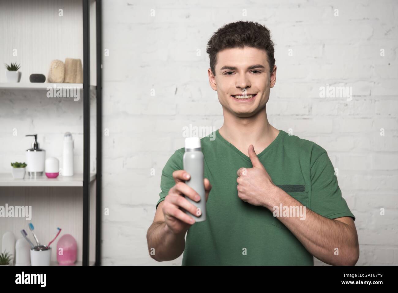 smiling young man showing thumb up while holding deodorant and looking at  camera Stock Photo - Alamy