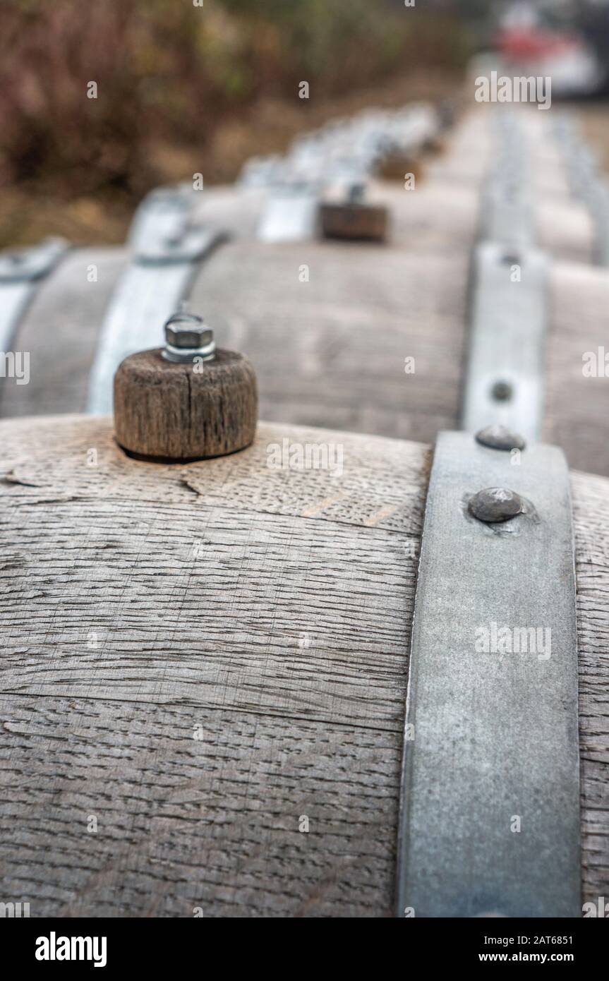 Macro photograph of small vintage grey wooden wine barrels in a long row in winter season. Shot in daylight at St. Claire's Vineyard, Botanical garden Stock Photo