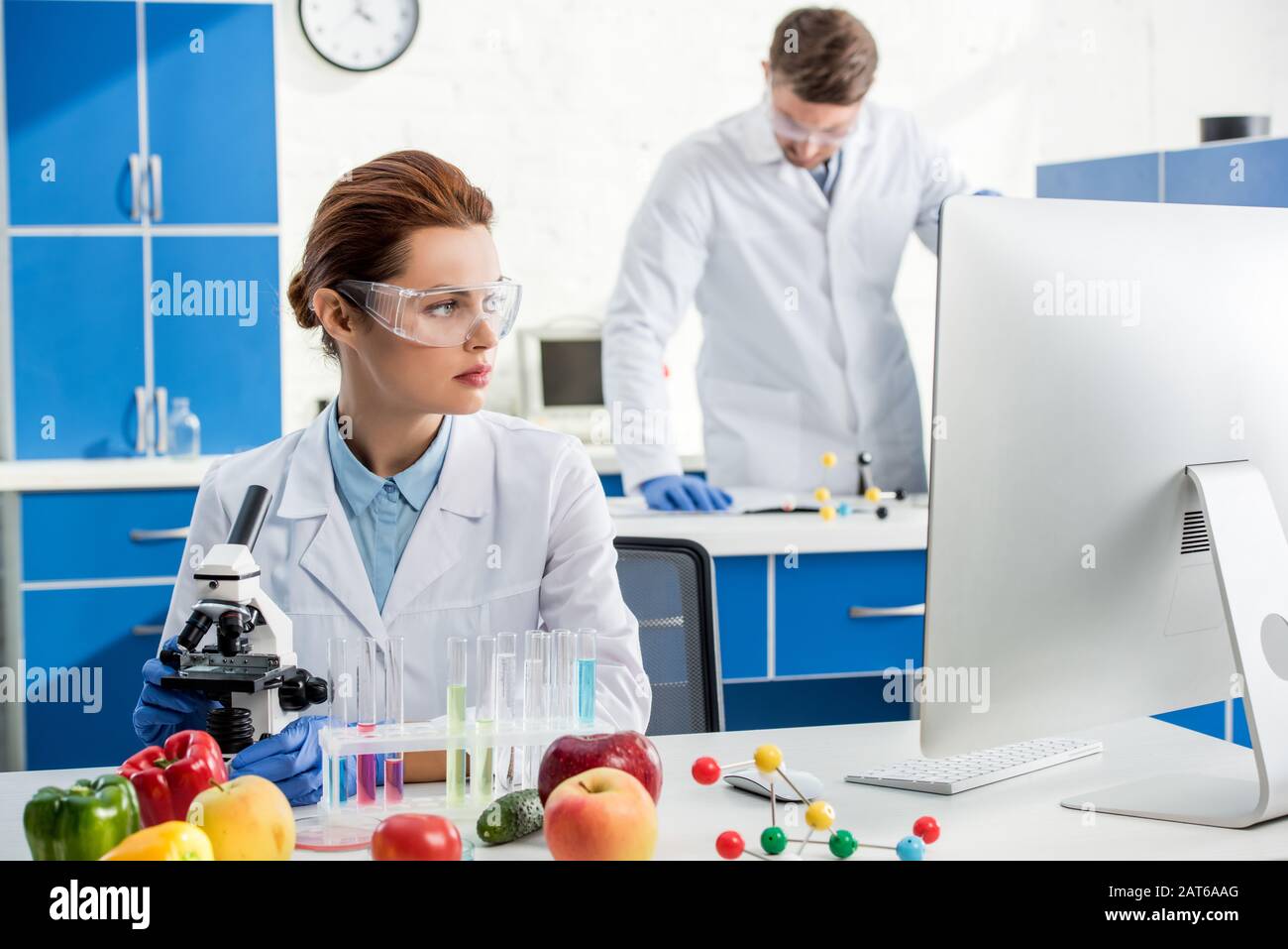 selective focus of molecular nutritionist looking at computer and colleague on background Stock Photo
