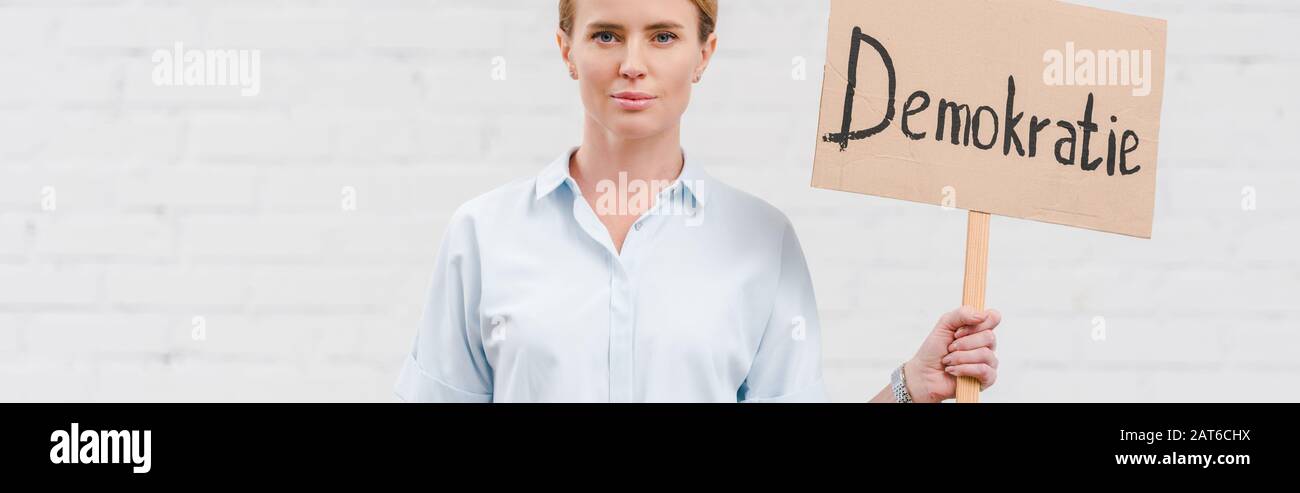 panoramic shot of woman holding placard with demokratie lettering near brick wall Stock Photo
