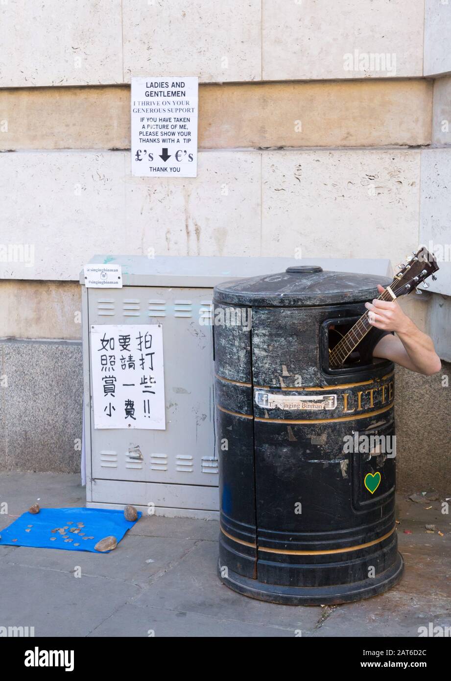 Street busker hiding in rubbish bin playing a guitar, in Cambridge, UK Stock Photo
